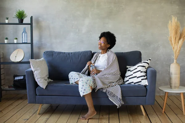 Jovem afro-americana feliz sentar relaxar no sofá acolhedor feliz para se mudar para novo apartamento. Sorrindo menina negra descansar no sofá confortável na sala de estar sonhando — Fotografia de Stock