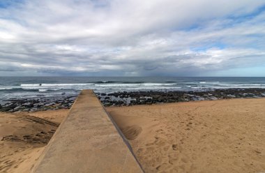 Kayalık sahil ve mavi bulutlu kıyı Peyzaj görüntüsü, Durban, Güney Afrika Garvies plajda karşı kumlu plaj üzerine uzanan beton drenaj boru hattı