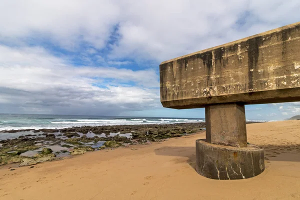 Concrete drainage pipeline extending onto sandy beach against rocky shoreline and blue cloudy coastal landscape at Garvies beach on the Bluff,  Durban, South Africa