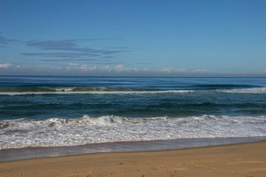 Mavi gökyüzü ve ufukta bulutlarla dolu bir sahil.
