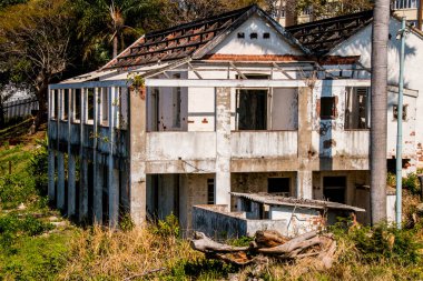 Terk edilmiş beyaz ev, yarı yıkım halinde. Etrafı bitkilerle çevrili.