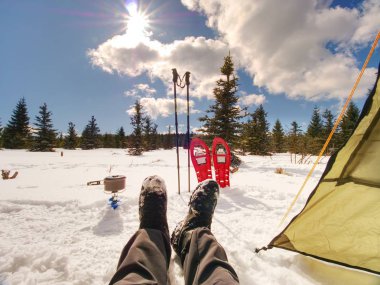 Yemek pişirme ve kış iz sırasında oturan adam. Kar ayakkabılarını ve Polonyalılar yeşil çadır yakınındaki kar üzerinde durun. Bir kış yürüyüş için donatım. 