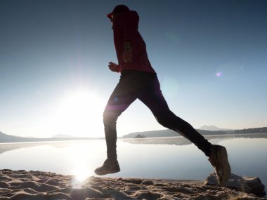 Güzel bir gün batımı zemin karşı sahilde koşan adam. Kum derin ayak izleri ile dağ gölü.