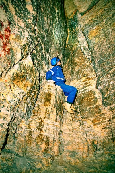 Man in dark old tunnel, indoor shoot. Stairs to the tunnel with walls made of orange sand stone. Staff in blue overall and safety helmet.