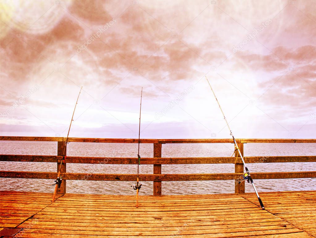 Abstract effect.  Several fishing rods against the wooden railing of the beach pier. Overcast day, with the hidden sun.