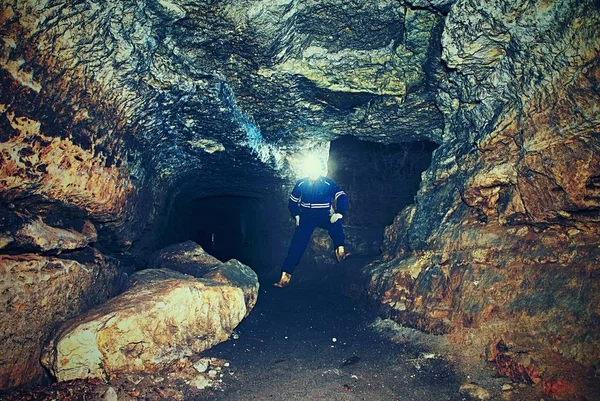 Man in dark old tunnel, indoor shoot. Stairs to the tunnel with walls made of orange sand stone. Staff in blue overall and safety helmet.