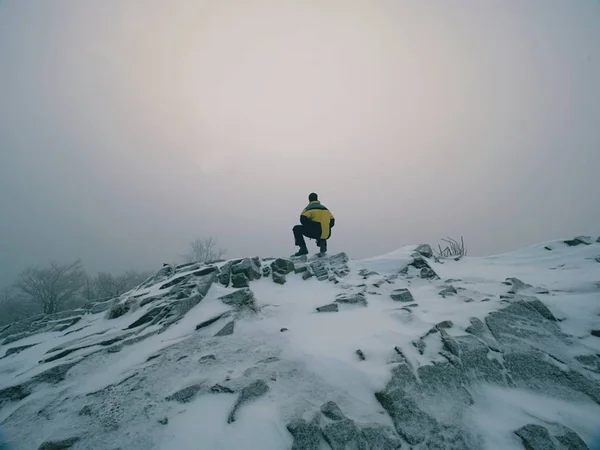 Winter misty landscape. Tourist with warm clothes stay in heavy fog on frozen rocky peak. National park.