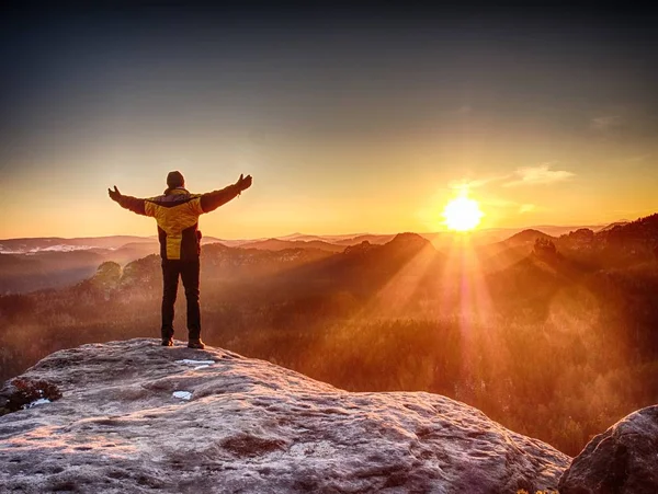 Man standing at the rocky edge. Young man watching sunrise  at hilly horizon. Exposed  peak of rock above foggy valley.