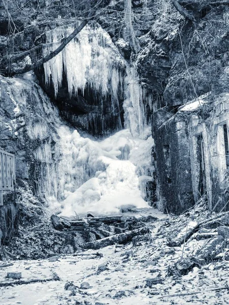 Frozen waterfall between rocks. Fallen icicle bellow waterfall, stony and mossy stream bank.
