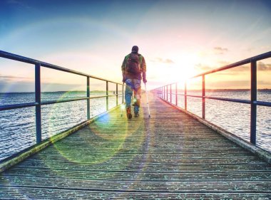 Adam ahşap İskelede güneşin doğuşunu gider. İskele inşaat deniz yukarıda güneş fantastik sabah açık gökyüzü yumuşak su seviyesi ile takip