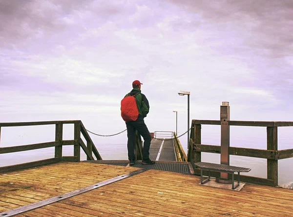 Back view of tourist in trekking clothes on sea  wooden pier. Gradient  misty view
