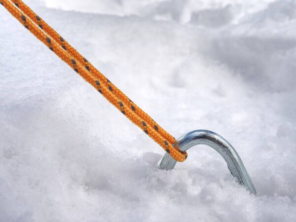 Detail of tent nylon strap anchored into snow.  Camping in wild nature park in early spring. Adventure travel active lifestyle freedom outdoors.