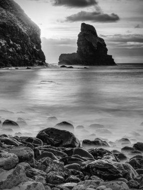 Akşam Bay. Keskin kayalara, siyah yuvarlak kayalar, taşlık Plajı, kum ve karanlık gökyüzü.