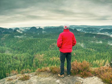 Adam turist cliff üzerinde. Uzun yürüyüşe çıkan kimse kırmızı ceketli kadar zirveye tırmandı görünümü keyfini çıkarın. Dağcı sıcak kırmızı ceketli dağlık manzara seyretmek