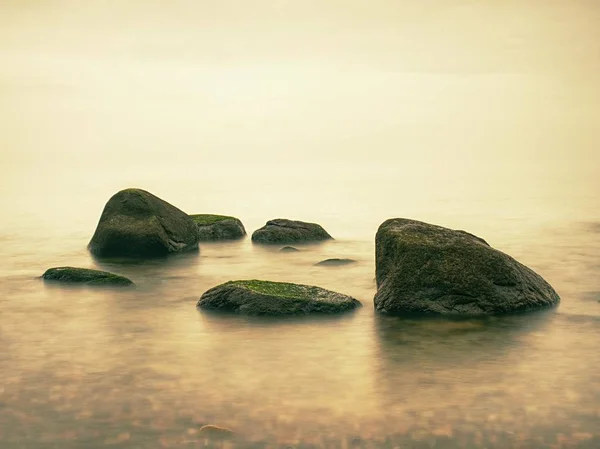 石の海岸は 高湿度のぼやけた太陽と海空の波に挑みます 滑らかな夜海石と地平線の間 静かな穏やかな水と穏やかな背景 — ストック写真