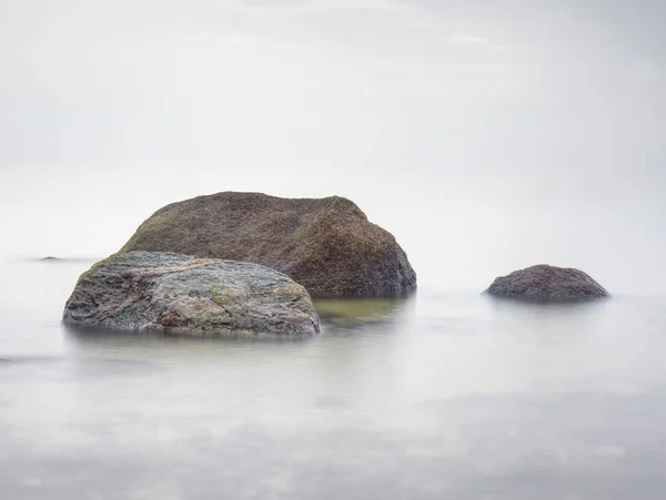 石の海岸は 高湿度のぼやけた太陽と海空の波に挑みます 滑らかな夜海石と地平線の間 静かな穏やかな水と穏やかな背景 — ストック写真