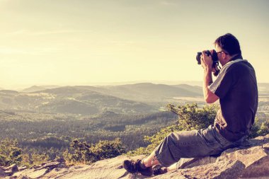 Doğa fotoğrafçısı manzara siste kirlenmiş bir dağ cliff alarak resim üzerinde. Turist ile fotoğraf makinesi ve tripod soğuk havalarda