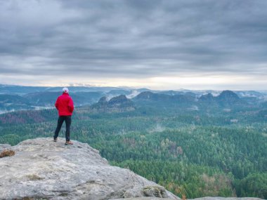 Yalnız kumtaşı kaya ve güneş Misty ve Sisli sabah Vadisi için bekleyen kürsüye sıcak kırmızı ceket uzun yürüyüşe çıkan kimse