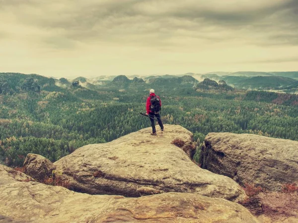 单独徒步旅行者在温暖的红色夹克站立在砂岩岩石的高峰和等待太阳 薄雾朦胧的清晨山谷 — 图库照片
