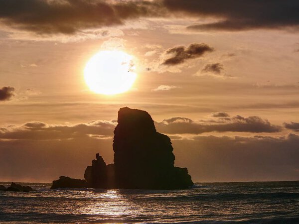 Beautifully shaped black boulders and a dramatic fiery sunset and a stony beach