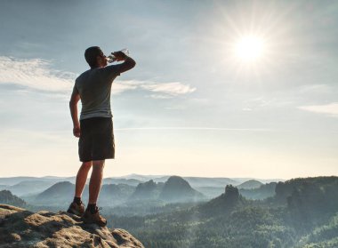 Miidle yaş adam içme suyu üzerinde kayalık zirve plastik şişe. Saf doğa egzersiz kavramı.