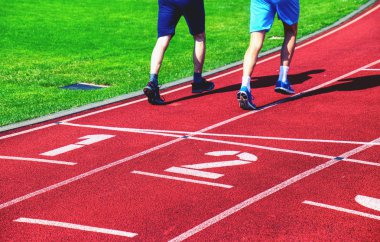 Erkek sporcular açık stadyum yolda çalıştırıyorsunuz. Kırmızı lastik koşma parça numaraları ve wwhite çizgili stadyum.