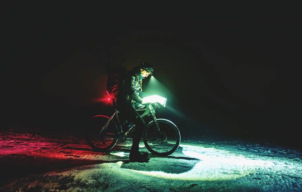 Конкурент зимней ночной гонки mtb остановки для возможного контроля. Байкер с белым жирным велосипедом смотрит на карту ночью во время снега
. 