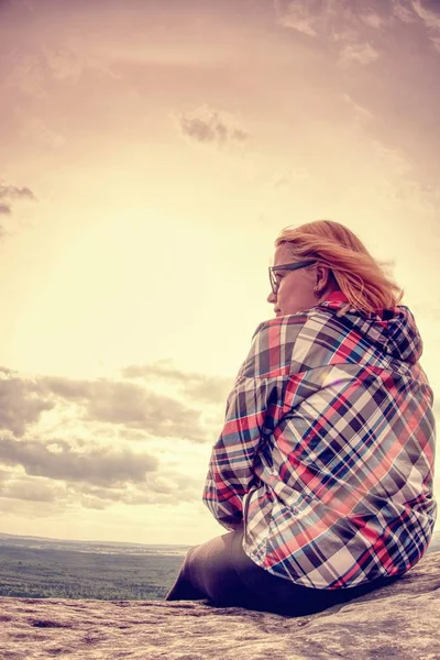 Genç kız turist uçurumun kenarında oturur ve Dağları'nın eteklerinde orman bakar. Rüzgarlı bir gün ile clounds arasında gizli güneş. 