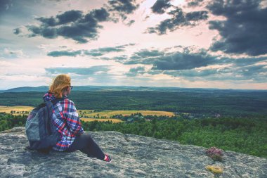 Genç kız turist uçurumun kenarında oturur ve Dağları'nın eteklerinde orman bakar. Rüzgarlı bir gün ile clounds arasında gizli güneş. 