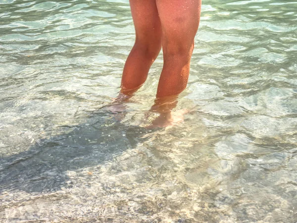 Naked legs along wave of lake water and rough white stony sand on the beach. Carefree and relaxing attitude