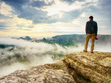 Photograper elinde kamerayla hazır manzara. Adam Güz fotoğraflar için maruz kalan kaya üzerinde dijital kamerası ile tırmandım. Cliff sisli sonbahar manzara yukarıda.