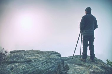 Doğa fotoğrafçısı manzara siste kirlenmiş bir dağ cliff alarak resim üzerinde. Turist ile fotoğraf makinesi ve tripod soğuk havalarda