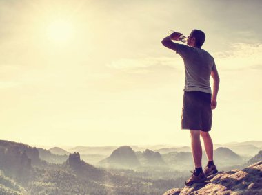 Şeffaf şişeden içme yolunun terli susuz oyundaki. Vahşi dağlık manzara. Adam şort ve beyaz elbise