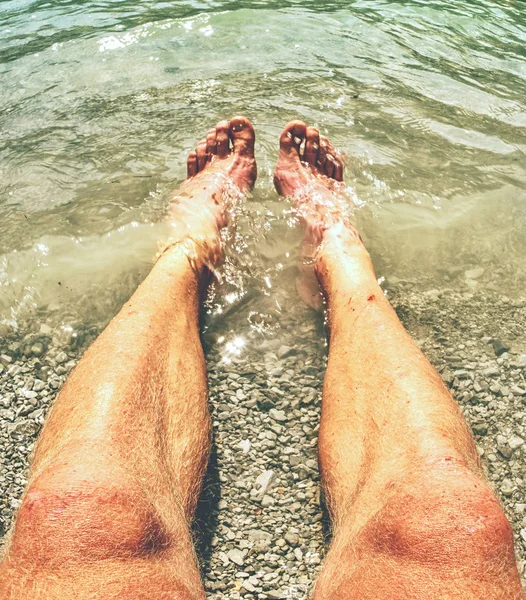 Hairy strong male legs are cooling in cold water of mountain lake. Green blue cold water of kaje in Dolomiti.