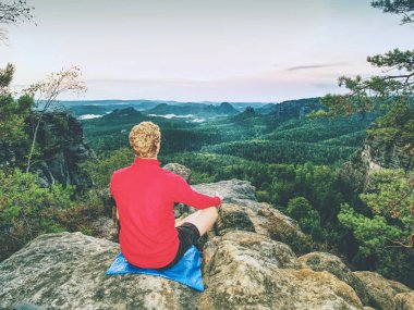 Yoga yapan adam orning içinde kayanın üzerinde poz veriyor. Orta yaşlı sporcu lüks manzaralı dağlarda yoga ve meditasyon yapıyor.