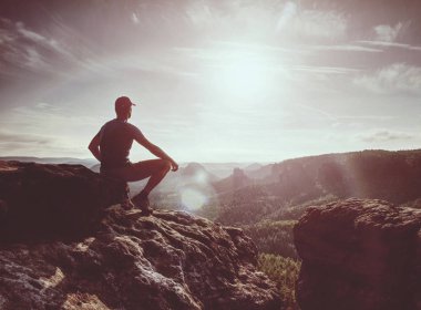 Fiyatı siyah kayalık tepe üzerinde. Gün doğumuna dağlarda derin vadi sis. Adam kayanın üzerinde oturmak.