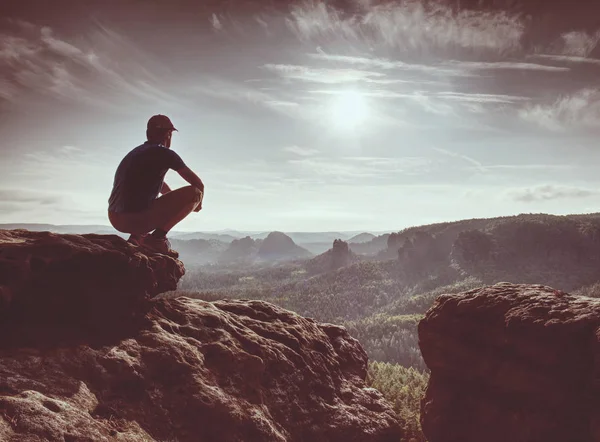 岩が多い峰の黒のハイカー 夜明けの山 深い谷の霧 男は岩の上に座る — ストック写真