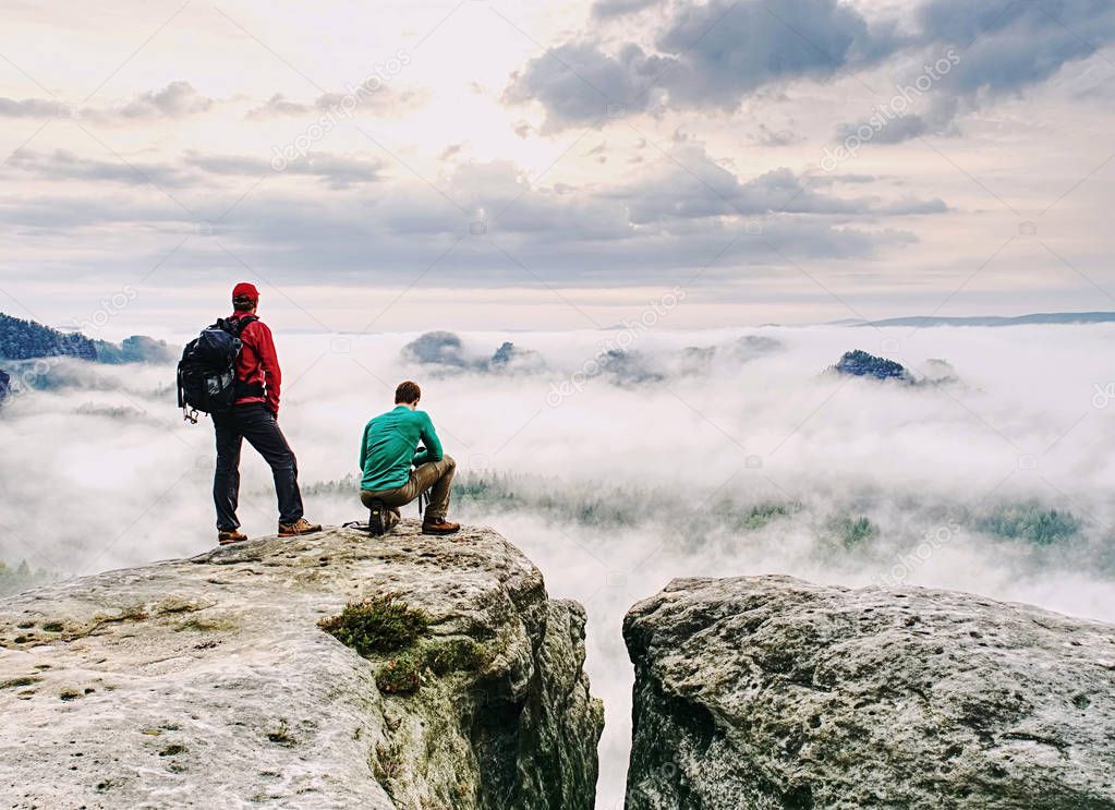Hiker and photographer with camera stay on cliff and takes photos. Autumn nature, misty landscape cloudy sky.