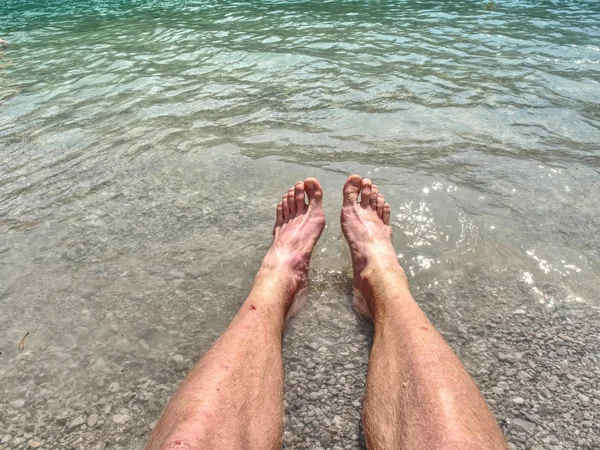 Hairy strong male legs are cooling in cold water of mountain lake. Green blue cold water of kaje in Dolomiti.
