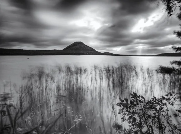 Autumn view over  low level pond to forest hill on opposite bank. Autumn melancholic atmosphere. Long exposure.   Black and white photo.