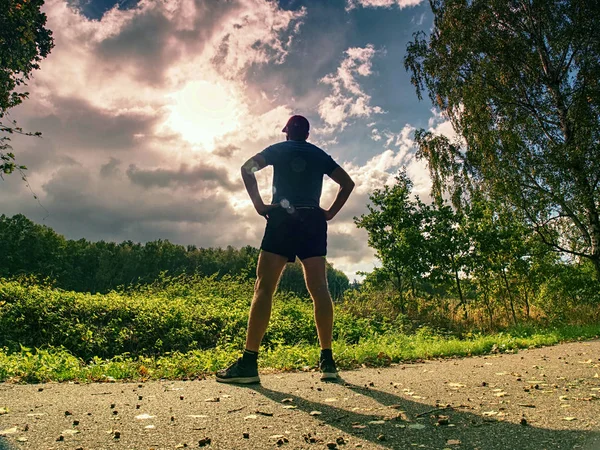 Jogging tall sports man in trees shadows with sun light behind him while wearing black yellow shorts and blue jogging attire