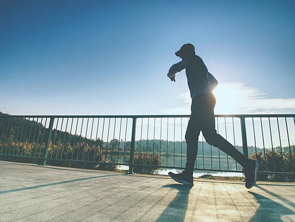 Tall slim man run on the lake terrace against the backdrop of a beautiful sunrise. Shore of mountain lake with dark forest hills