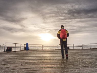 Arkadan görünüşü backpacker turist nehir ve karanlık gökyüzü arka plan önünde ahşap iskele üzerinde. Tatil kavramı üzerinde seyahat 