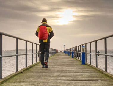 Arkadan görünüşü backpacker turist nehir ve karanlık gökyüzü arka plan önünde ahşap iskele üzerinde. Tatil kavramı üzerinde seyahat 