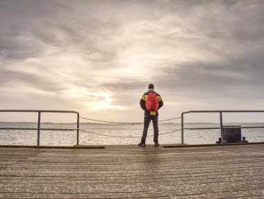 Arkadan görünüşü backpacker turist nehir ve karanlık gökyüzü arka plan önünde ahşap iskele üzerinde. Tatil kavramı üzerinde seyahat 