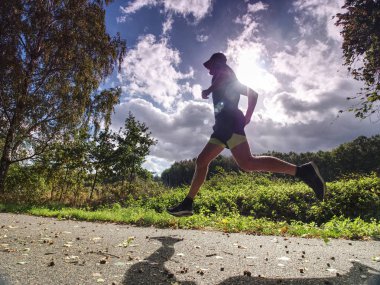 Ağaçlar gölgeler güneş siyah sarı şort ve mavi jogging kıyafetleri giyerken onu ışık ile erkekte uzun boylu spor koşu