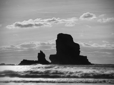 Güzel siyah kayalar ve dramatik bir ateşli günbatımı ve taşlı bir plaj şeklinde