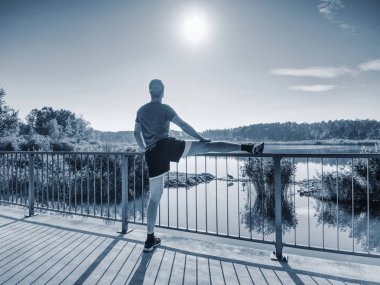 Adam içinde güneşli sabah dışında çalışma gitmeden önce bacaklarını germe. Kasları ısınma. Açık göl köprüde egzersiz.