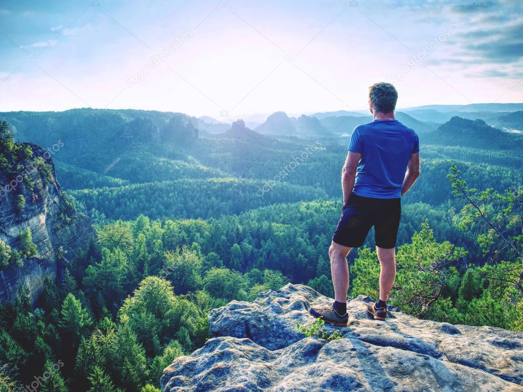 Man on a stone observing the landscape. Lonely young sportsman stands on the mountain and looks into the far distance 
