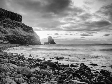Akşam Bay. Keskin kayalara, siyah yuvarlak kayalar, taşlık Plajı, kum ve karanlık gökyüzü.